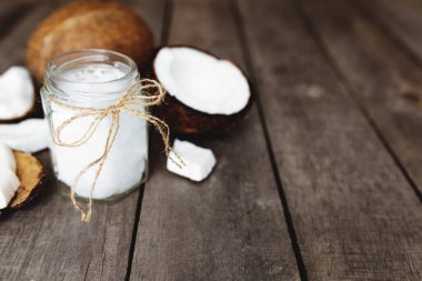 Kırık hindistan cevizleri, gri ahşap arka planda, yağ kavanozuyla. Beyaz hindistan cevizi hamuru