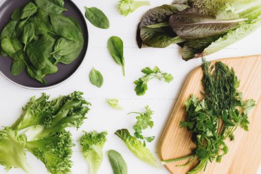 Kesme tahtası, taze yeşil salata yaprakları, ıspanak, marul, romaine ve maydanozla bembeyaz arka planda fesleğen. Sağlıklı vejetaryen yeme konsepti. Yüksek kalite fotoğraf