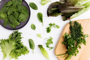 Kesme tahtası, taze yeşil salata yaprakları, ıspanak, marul, romaine ve maydanozla bembeyaz arka planda fesleğen. Sağlıklı vejetaryen yeme konsepti. Yüksek kalite fotoğraf