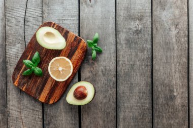 Sağlıklı beslenme konsepti düzdü. Akdeniz diyeti, avokado yarımları, çekirdek, fesleğen ve ahşap arka planda limon yarısıyla kesim tahtası. Vejetaryen yemeği. Sağlıklı gıda konsepti. Organik yiyecekler