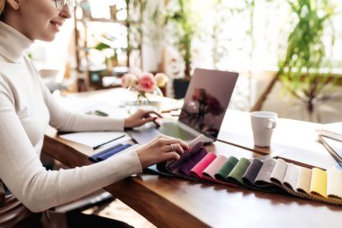 Bir iç mimar yeni bir proje üzerinde çalışıyor. Yeni mobilyalar için kumaş rengi paletinden renk seçiyorum. Meşe ağacından masa. Bir fincan kahve, vazodaki çiçekler mutlu müşterilerden. Yüksek kalite fotoğraf