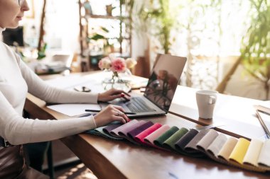 Bir iç mimar yeni bir proje üzerinde çalışıyor. Yeni mobilyalar için kumaş rengi paletinden renk seçiyorum. Meşe ağacından masa. Bir fincan kahve, vazodaki çiçekler mutlu müşterilerden. Yüksek kalite fotoğraf