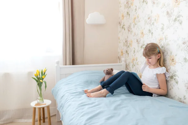 Маленька Дівчинка Сидить Ліжку Стильній Спальні Читає Блакитну Книгу Освіта — стокове фото