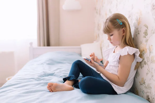 Kız yatakta oturuyor, elinde telefonla bir şeyler okuyor.