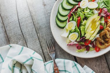 Sağlıklı beslenme konsepti havlu ve çatalla yatıyordu. Akdeniz diyeti, marul salatası yapraklı tabak, bıldırcın yumurtası, dilimlenmiş avokado, domates, salatalık, kırmızı tatlı biber, ahşap arka planda fesleğen.