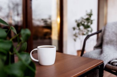 Gün batımında, arka planı bulanık bir şekilde, ahşap kahverengi terasın üzerindeki masada bir fincan kahve ya da çay. Rahatlama, sessiz kır hayatı konsepti