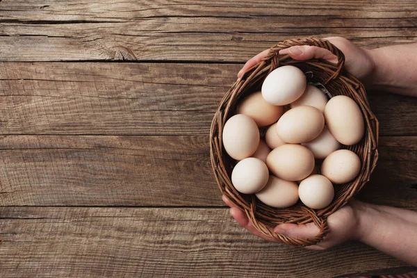 Tahta arka planda organik tavuk yumurtalarıyla el ele tutuşma sepetiyle yatıyordu. Serbest tarım ve otlaktan gelen yumurtalarla birlikte organik ev konsepti tavuklar yetiştirdi.