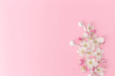 Elma çiçeği süsü ve kulaklıklarla pembe arka planda yatıyordu.