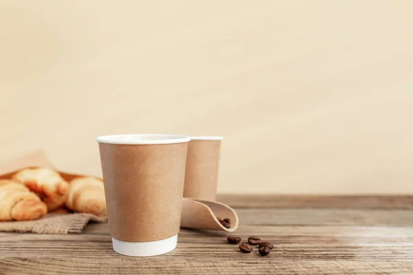 Dua cangkir kertas kopi, croissant, biji kopi dan sendok di meja kayu — Stok Foto