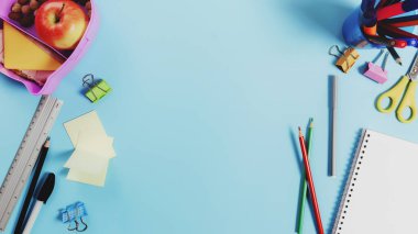 İlkokul dairesi konsepti çeşitli okul malzemeleri, not defteri, kalem, piyasa, çıkartmalar, ataçlar, sandviç, fındık ve elma ile mavi arka planda.