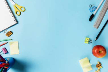 Okul aksesuarları, kalemler, kalem, not defteri, ataç, elma, fındık, cetvel, makas, mavi arka planda kağıt çıkartması gibi çeşitli okul aksesuarları, iş veya eğitim kavramlarıyla yatıyordu