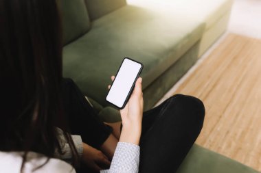 Siyahlarla iletişim konsepti yeşil koltukta oturan ve elinde beyaz bir ekranla akıllı telefon tutan, ön tarafta güneş ışığı olan bir kız.