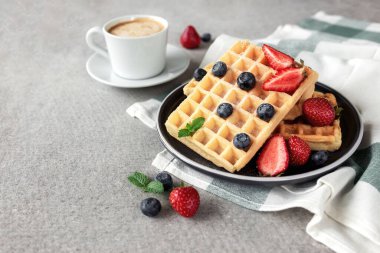 Waffle tabağı, çilek, yabanmersini, nane yaprağı, gri arka planda kahve fincanı.