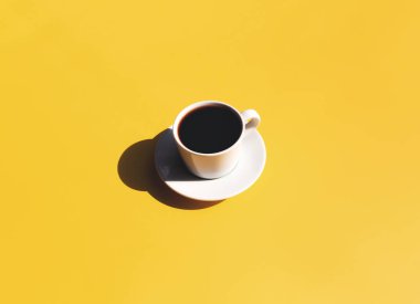 Tek beyaz kupa ve siyah espresso tabağı. Üstten bakıldığında, sarı bej arka planda, güneşin gölgesi olan kahve. Yüksek kalite fotoğraf