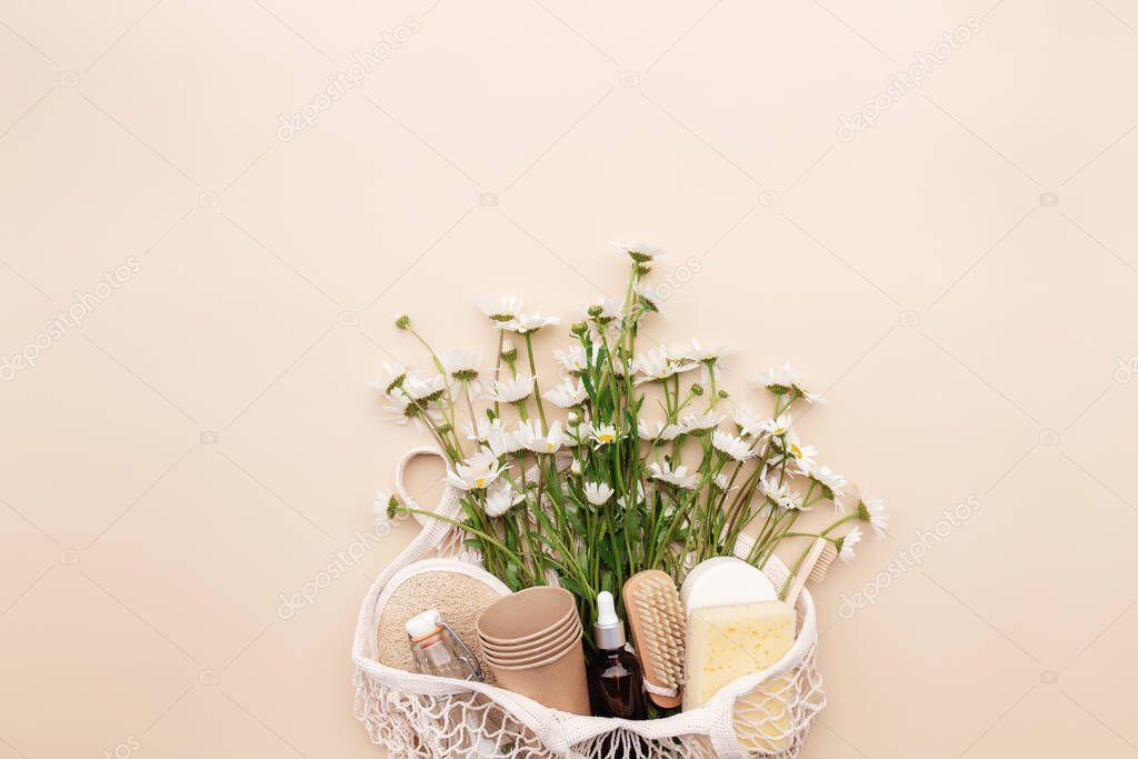 Eco friendly summer concept on beige background with eco shopping bag, white chamomile flowers, bath accessories, brushes, essential oil bottle, soap and sponge inside. High quality photo