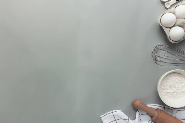 Выпечка ингредиенты, кухонная утварь, кулинарная концепция на сером фоне плоский лежал, копировать пространство. Приготовьте тесто, яйцо, муку из миски, скалку, венчик, кухонное полотенце, соль, содовую. Кухня как хобби