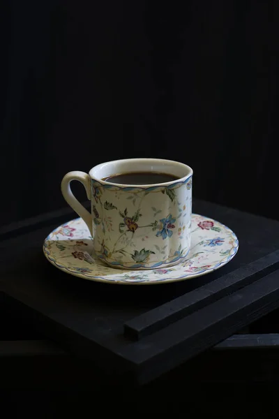 Kahveli eski beyaz seramik bardak koyu bir arka planda ahşap bir ayakta duruyor.