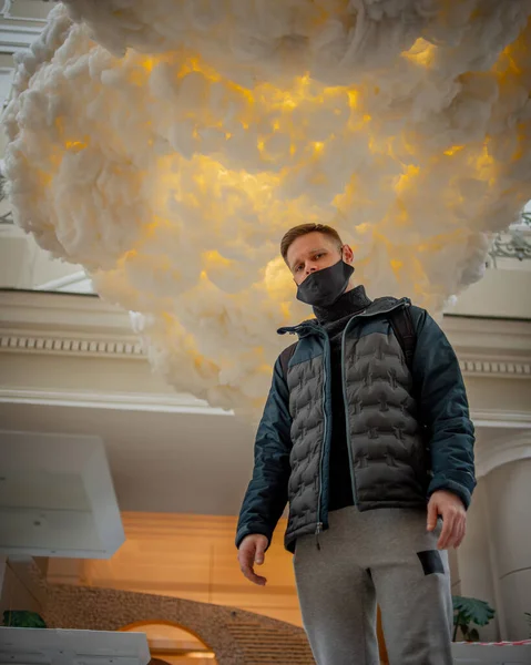 Yüzünde siyah bir maske olan bir adam bulutun arka planında duruyor.