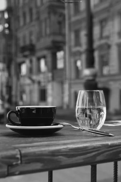 Ön planda, masanın üzerinde, bir fincan kahve ve bir bardak su var.