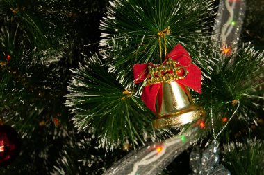 Koyu yeşil bir Noel ağacına asılı kırmızı kurdeleli altın çan şeklinde bir Noel ağacı oyuncağı. Yeni yıl. Noel zamanı. kopyalama alanı. Yatay. yakın plan. 