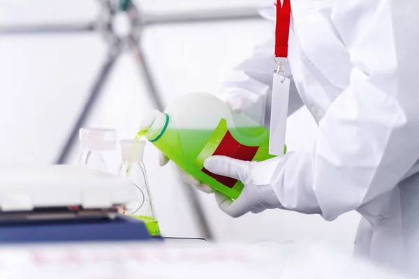 Beyaz önlüklü adam yeşil sıvı döküyor. 