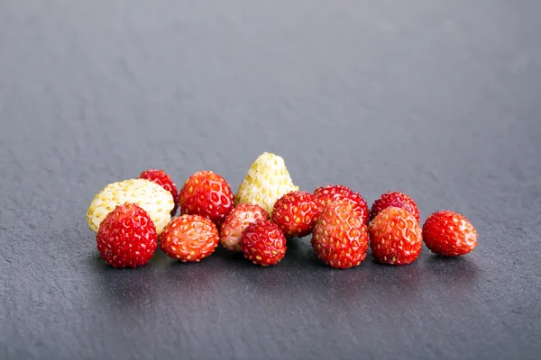 Hoop van kleine rijpe rode en witte wilde aardbeien op leisteen zwart — Stockfoto