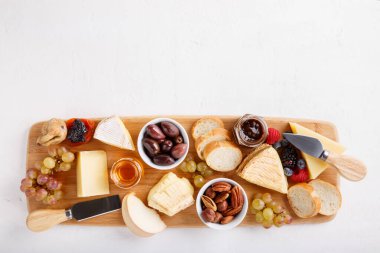 Cheese plate. French cheese with nuts, grape, berries, dried fruits and honey on cutting board on white. Camembert, Livarote, Pont-L'eveque cheese from Normandy and comte cheese. Top view. clipart