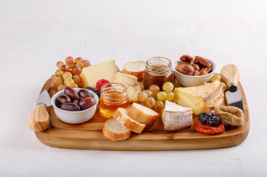 Cheese plate. French cheese with nuts, grape, berries, dried fruits and honey on cutting board on white. Camembert, Livarote, Pont-L'eveque cheese from Normandy and comte cheese.  clipart