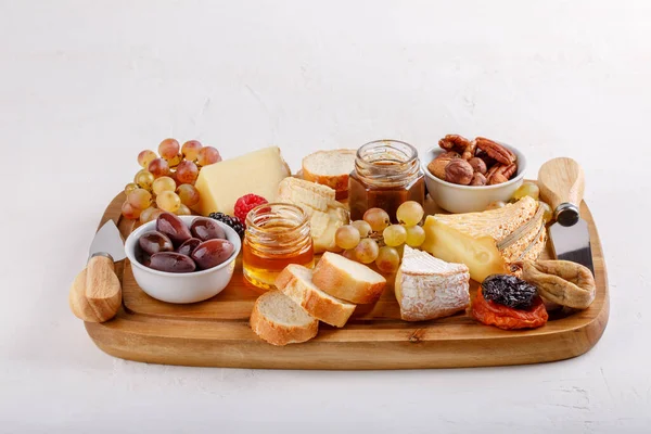 Cheese plate. French cheese with nuts, grape, berries, dried fruits and honey on cutting board on white. Camembert, Livarote, Pont-L\'eveque cheese from Normandy and comte cheese.