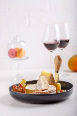 Peynir tabağı ve kırmızı şarap, siyah peynir tabağı beyaz masada.. 