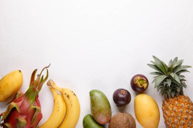 Beyaz üzerine tropik meyveler. Ejderha meyvesi, mango, ananas, mangosteen, muz, hindistan cevizi. Sağlıklı yemek geçmişi. Yaz kavramı. Üst görünüm, kopyalama alanı, düz uzanma.