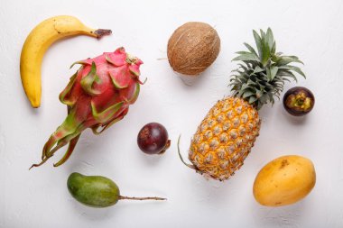 Beyaz üzerine tropik meyveler. Ejderha meyvesi, mango, ananas, mangosteen, muz, hindistan cevizi. Sağlıklı yemek geçmişi. Yaz kavramı. Üst manzara, düz uzanma.