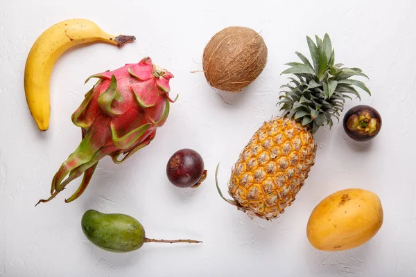 Beyaz üzerine tropik meyveler. Ejderha meyvesi, mango, ananas, mangosteen, muz, hindistan cevizi. Sağlıklı yemek geçmişi. Yaz kavramı. Üst manzara, düz uzanma.