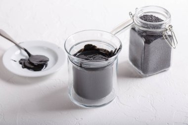 Beyaz arka planda cam kavanozda siyah tahini sosu. Siyah susam tohumlarından yapılan doğal macun.. 