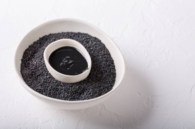 Siyah tahini sosu ve siyah susam tohumları beyaz arka planda kaselerde. Susam tohumundan yapılan doğal macun. Boşluğu kopyala.