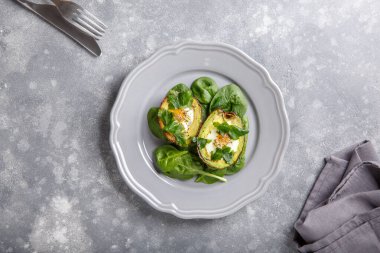 Avokadoda pişirilmiş bıldırcın yumurtası. Avokado yumurta tekneleri gri tabakta ıspanak yapraklarıyla servis edilir. Ketogenik, düşük karbonhidrat diyeti. Yemek arkaplanı. Üst Manzara. Boşluğu kopyala.