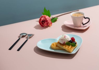 Kalp şeklinde Belçika waffle 'ı mavi tabakta ve bir fincan kahve pembe arka planda. Sevgililer Günün kutlu olsun..