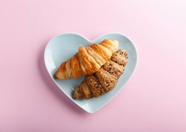 Pembe arka planda iki yeni pişmiş kruvasan. Üst Manzara. Boşluğu kopyala.