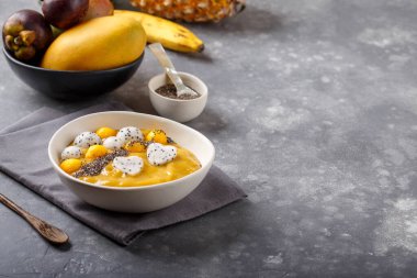 Gri arka planda meyve suyu kasesi. Chia tohumları, mango parçaları ve ejderha meyveleriyle kaplı lezzetli mango smoothie. Sağlıklı kahvaltı. Boşluğu kopyala.