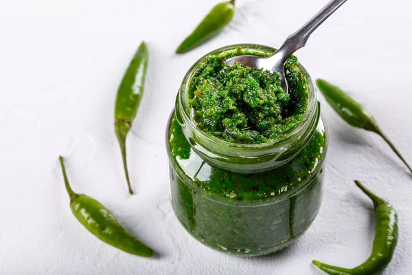 Acı biber ezmesi. Beyaz arka planda cam kavanozda yeşil sos. Gürcistan mutfağında Adjika veya ajika veya Arap mutfağında harissa.