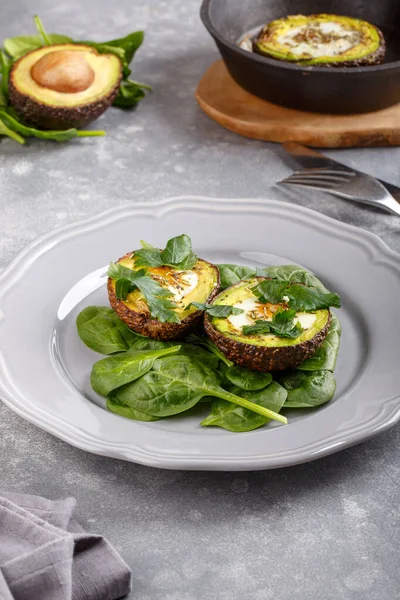 Quail eggs baked in avocado. Avocado egg boats served with spinach leaves on gray plate. Ketogenic, keto low carb diet.