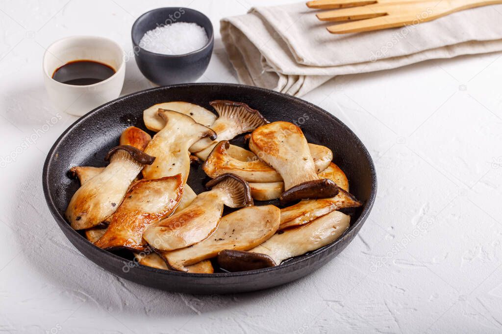 Fried eryngii mushrooms in cast-iron pan on white table. Grilled