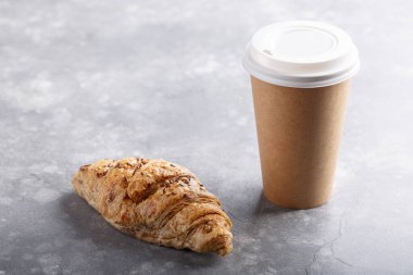 Kahvaltı için sabah kahvesi ve kruvasan. Kahveyi paket yap, kahvaltıyı da götür. Gri masadaki ekmekli kağıt bardak..