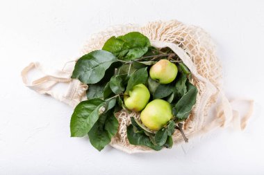 Beyaz arka planda ağlı alışveriş poşetinde yaprakları olan olgun yeşil elmalar. Üst görünüm.