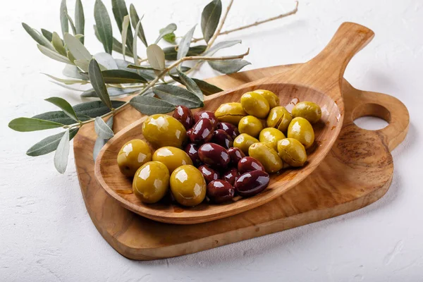 Different types of olives green and black on wooden plate on white table. Close-up.