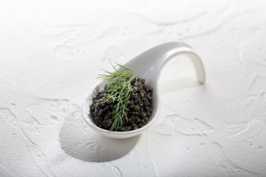 Beyaz arka planda siyah havyar. Mersin balıklı havyarlı seramik kaşık. Boşluğu kopyala.