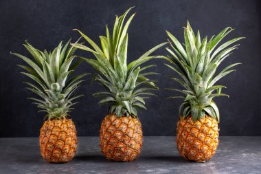 Arka planda üç tane taze olgun ananas var..