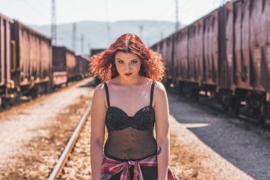 İki trenin arasında duran güzel kızıl saçlı kızın portresi.
