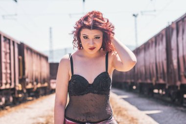 İki trenin arasında duran güzel kızıl saçlı kızın portresi.