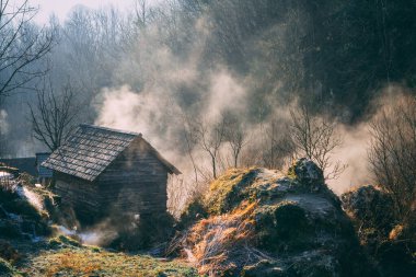 Bosna-Hersek 'in Krupa na Vrbasu kentindeki büyük kaya ve ormanlarla çevrili eski ahşap evin sabahın erken saatlerinde fotoğrafı
